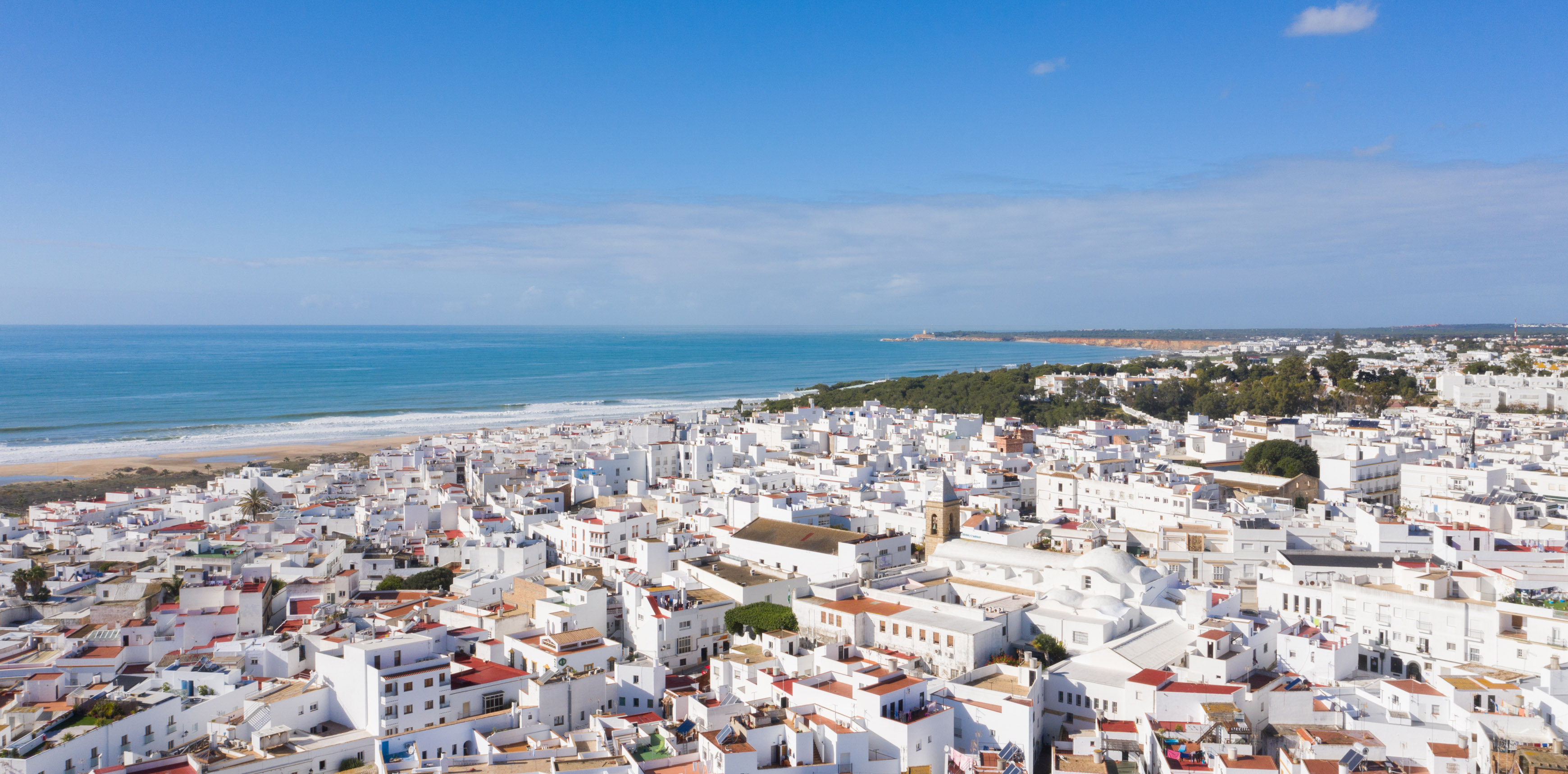 Weiße Häuser einer Küstenstadt mit Strand und Meer unter blauem Himmel